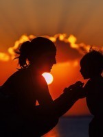 Mother holds child hands with sun setting in the background